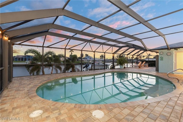 pool at dusk featuring a patio, a water view, and a lanai