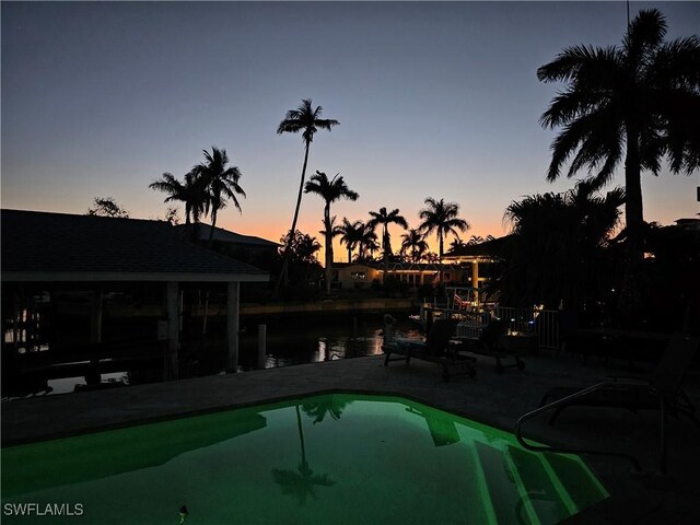 pool at dusk featuring a water view and a dock