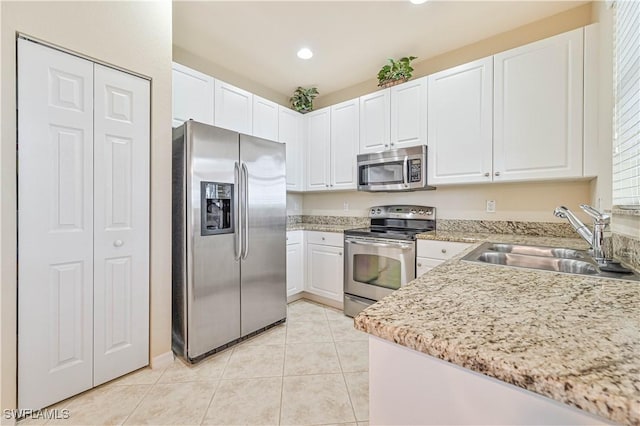 kitchen with light tile patterned floors, sink, white cabinets, stainless steel appliances, and light stone counters