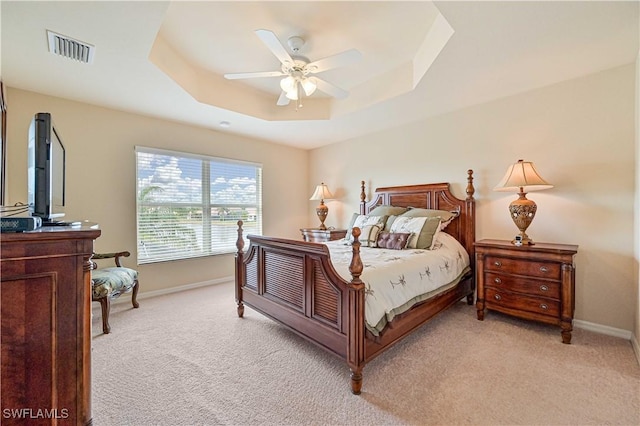 bedroom with ceiling fan, light colored carpet, and a tray ceiling