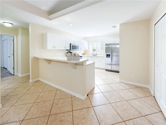 kitchen with light tile patterned floors, a breakfast bar area, stainless steel appliances, white cabinets, and kitchen peninsula