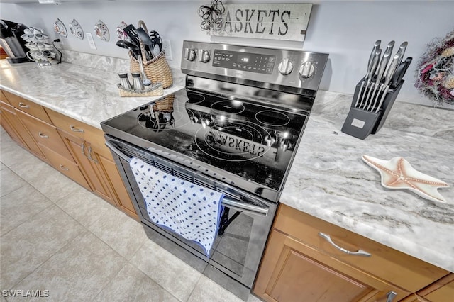 kitchen featuring light stone counters, stainless steel range with electric stovetop, and light tile patterned flooring