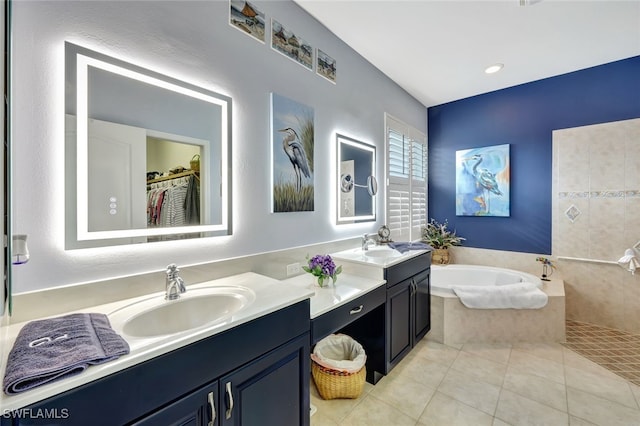 bathroom with tile patterned flooring, tiled tub, and vanity