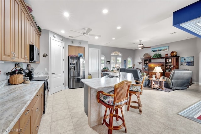 kitchen featuring light stone countertops, black range with electric stovetop, sink, stainless steel fridge with ice dispenser, and a breakfast bar area