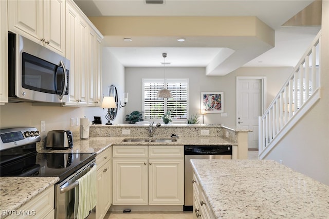 kitchen featuring sink, light stone counters, appliances with stainless steel finishes, pendant lighting, and cream cabinetry