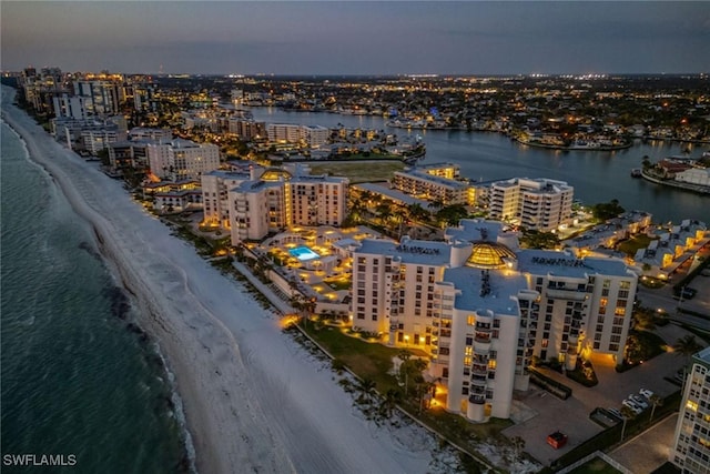 aerial view at dusk featuring a water view and a beach view