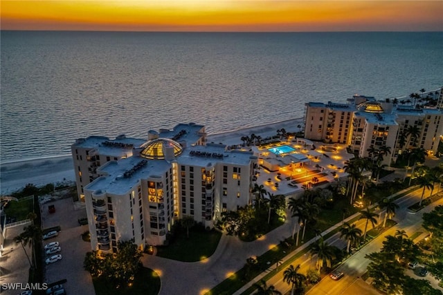 aerial view at dusk featuring a water view and a beach view