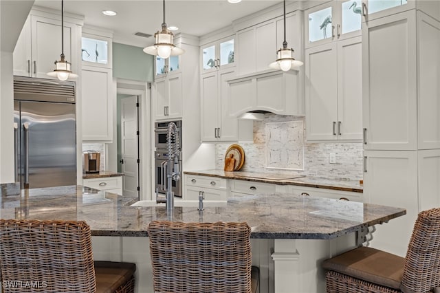 kitchen featuring a breakfast bar area, white cabinetry, dark stone counters, pendant lighting, and stainless steel appliances