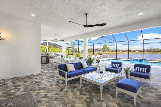 view of patio / terrace with a lanai, a water view, an outdoor living space, area for grilling, and an outdoor kitchen