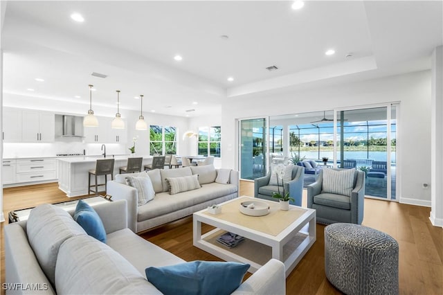 living room featuring a tray ceiling, sink, and light hardwood / wood-style flooring