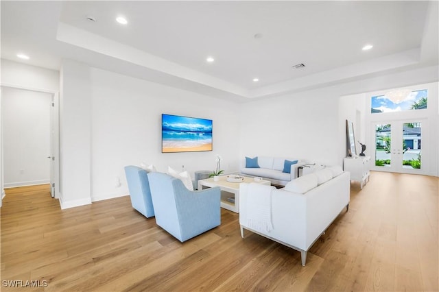 living room featuring a tray ceiling, light hardwood / wood-style flooring, and french doors