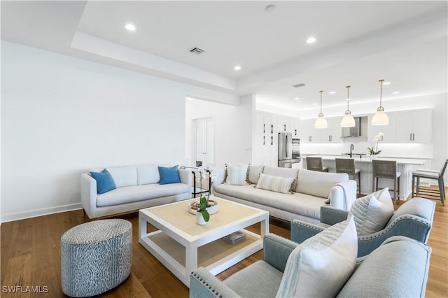 living room featuring a raised ceiling, sink, and light wood-type flooring