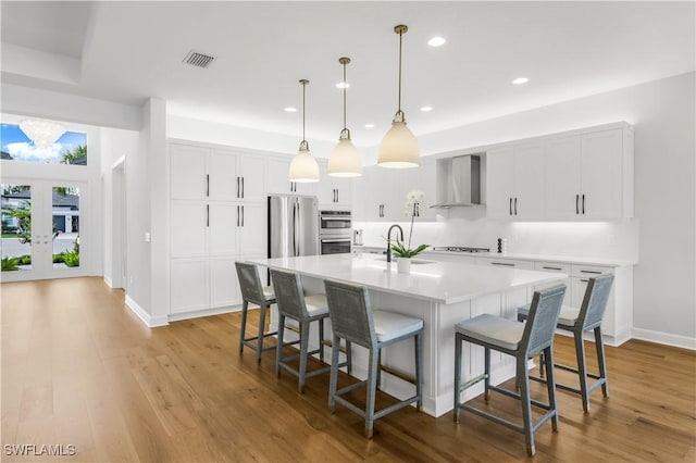 kitchen with pendant lighting, white cabinetry, an island with sink, a kitchen bar, and wall chimney exhaust hood