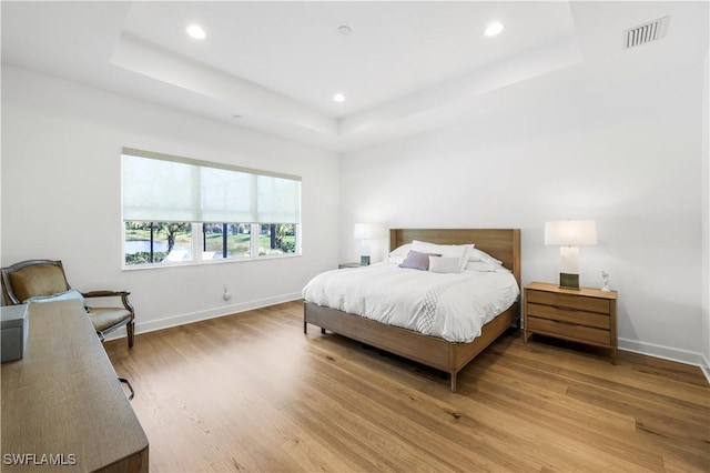 bedroom with wood-type flooring and a raised ceiling