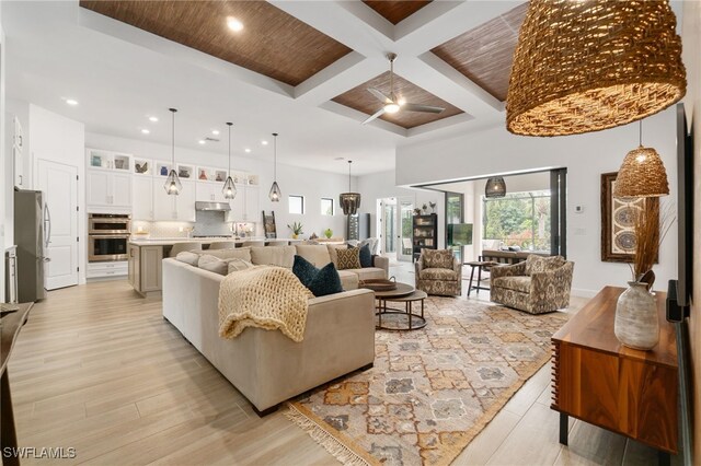 living room featuring coffered ceiling, beam ceiling, light hardwood / wood-style flooring, and a high ceiling