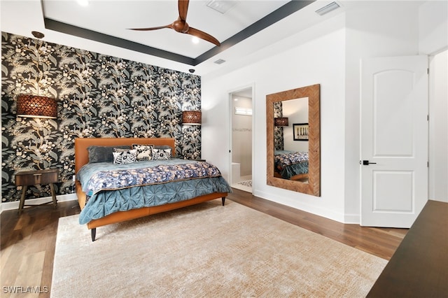 bedroom featuring connected bathroom, hardwood / wood-style floors, ceiling fan, and a tray ceiling