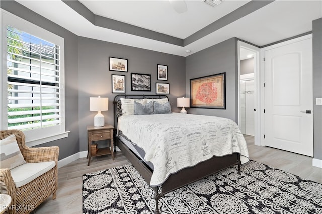 bedroom with a tray ceiling, ceiling fan, and light hardwood / wood-style flooring