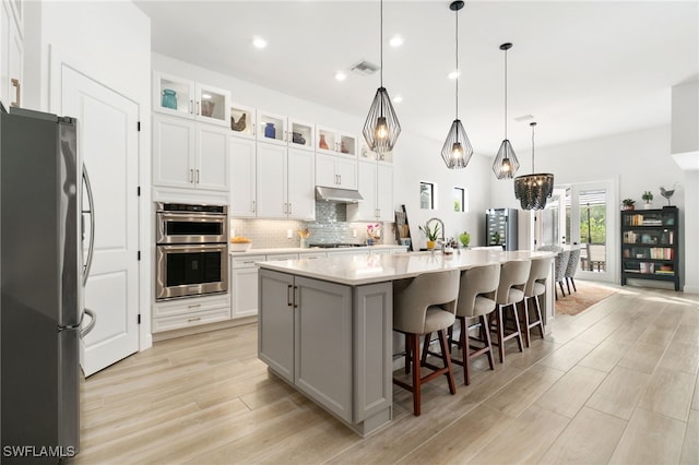 kitchen featuring white cabinetry, stainless steel appliances, an island with sink, and pendant lighting