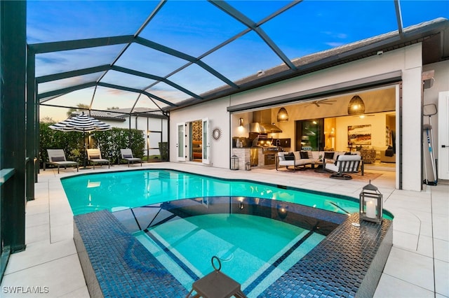 pool at dusk featuring a patio, glass enclosure, and exterior kitchen