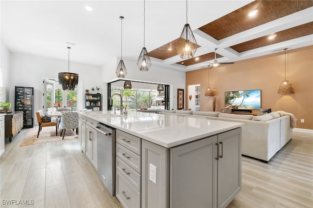 kitchen with sink, light stone counters, decorative light fixtures, stainless steel dishwasher, and an island with sink