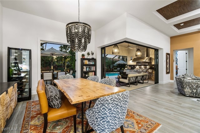 dining area with an inviting chandelier, beverage cooler, light hardwood / wood-style floors, and a high ceiling