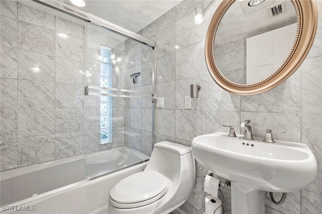 full bathroom with tile walls, sink, bath / shower combo with glass door, and toilet