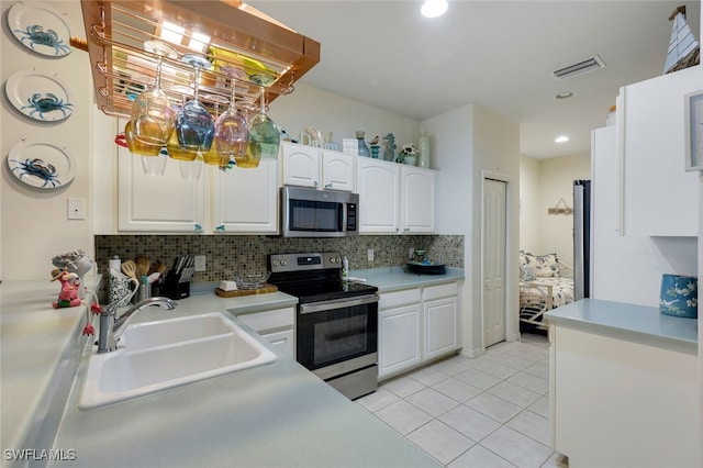 kitchen featuring appliances with stainless steel finishes, white cabinetry, tasteful backsplash, sink, and light tile patterned flooring