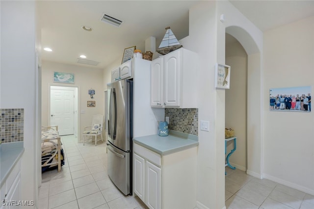 kitchen featuring backsplash, white cabinets, light tile patterned floors, and stainless steel refrigerator