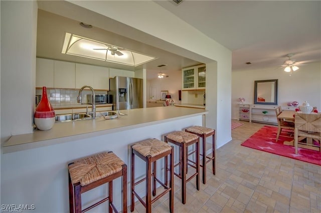 kitchen with sink, stainless steel fridge, a breakfast bar area, ceiling fan, and kitchen peninsula