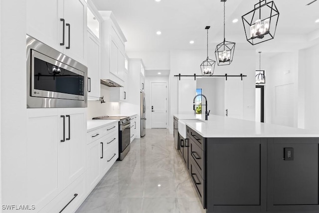 kitchen featuring a barn door, decorative light fixtures, stainless steel appliances, a large island, and white cabinets