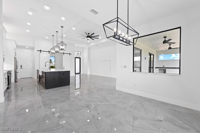 kitchen featuring hanging light fixtures, a barn door, white cabinets, and a center island with sink