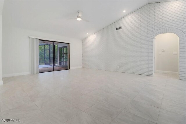 empty room with high vaulted ceiling, ceiling fan, and brick wall