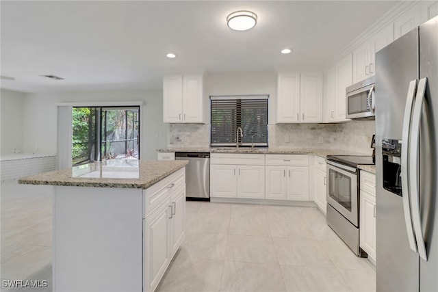 kitchen with appliances with stainless steel finishes, a center island, light stone countertops, white cabinets, and decorative backsplash