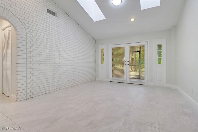 unfurnished room featuring lofted ceiling with skylight, brick wall, and french doors