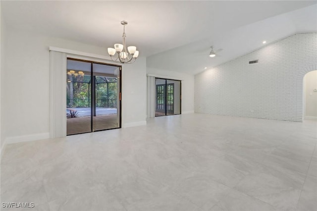 empty room with brick wall, ceiling fan with notable chandelier, and lofted ceiling