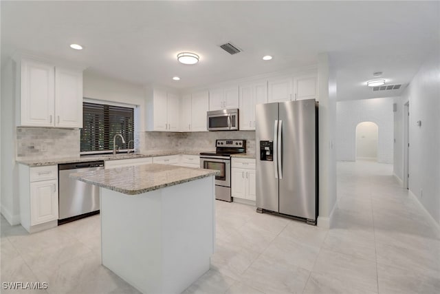 kitchen featuring sink, a center island, stainless steel appliances, light stone countertops, and white cabinets