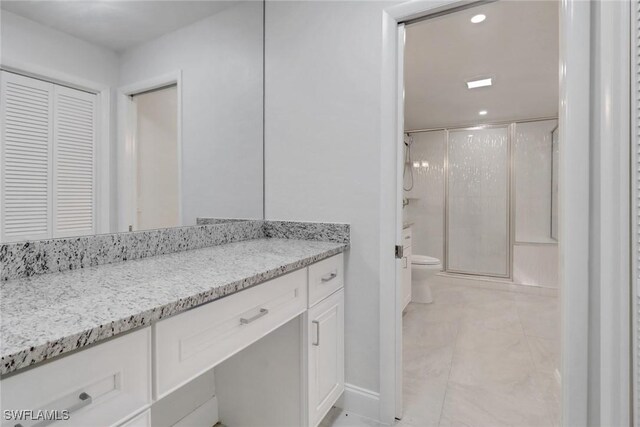 bathroom featuring toilet, vanity, and a shower with shower door