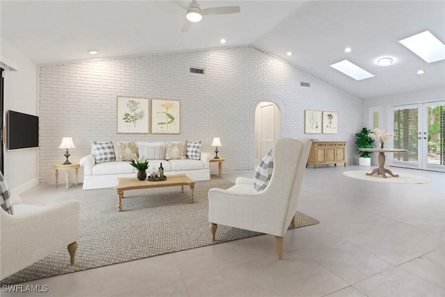 tiled living room featuring ceiling fan, french doors, vaulted ceiling with skylight, and brick wall