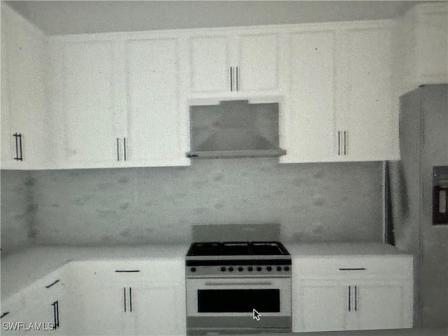 kitchen with backsplash, wall chimney exhaust hood, gas range gas stove, and white cabinets