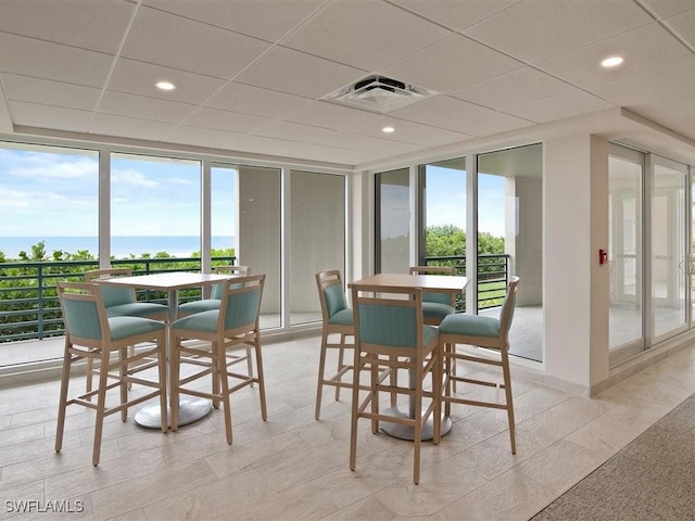 dining space with a water view, a paneled ceiling, floor to ceiling windows, and a wealth of natural light