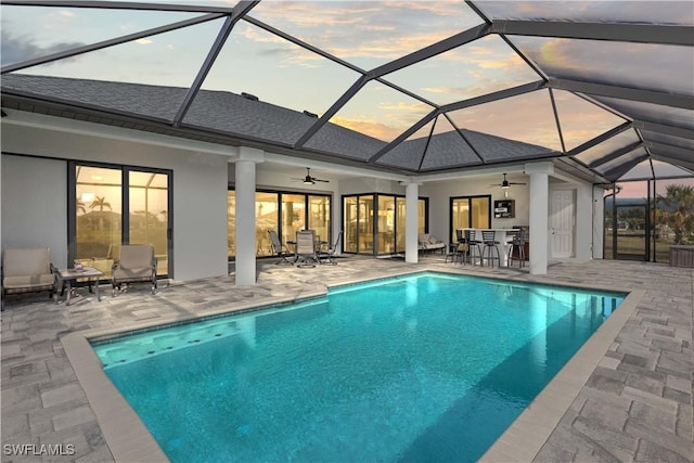 pool at dusk with ceiling fan, a lanai, and a patio