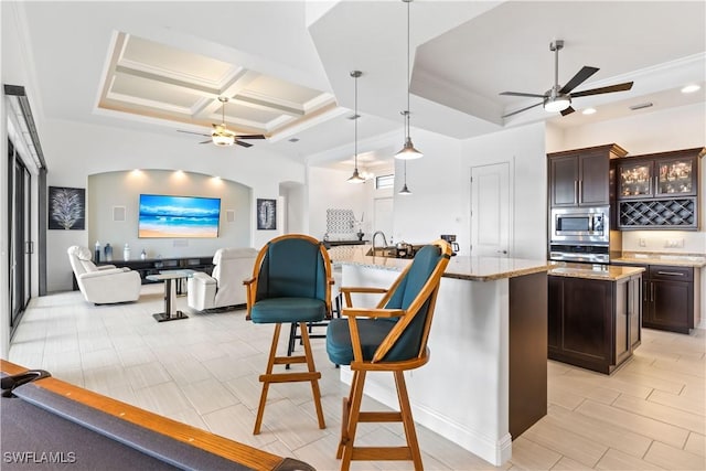 kitchen with ceiling fan, appliances with stainless steel finishes, dark brown cabinetry, a center island with sink, and decorative light fixtures