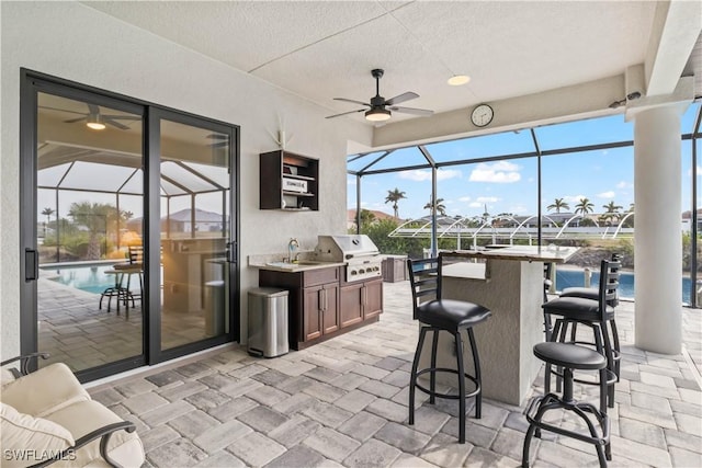 view of patio featuring an outdoor kitchen, a water view, grilling area, a lanai, and an outdoor wet bar