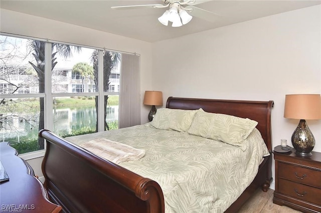 bedroom with light hardwood / wood-style flooring, ceiling fan, and a water view