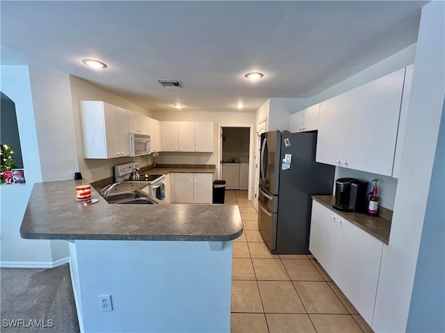 kitchen with white appliances, light tile patterned floors, white cabinets, kitchen peninsula, and independent washer and dryer