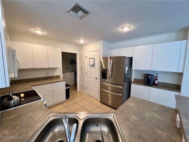 kitchen with separate washer and dryer, electric range oven, white cabinetry, stainless steel fridge with ice dispenser, and light tile patterned floors