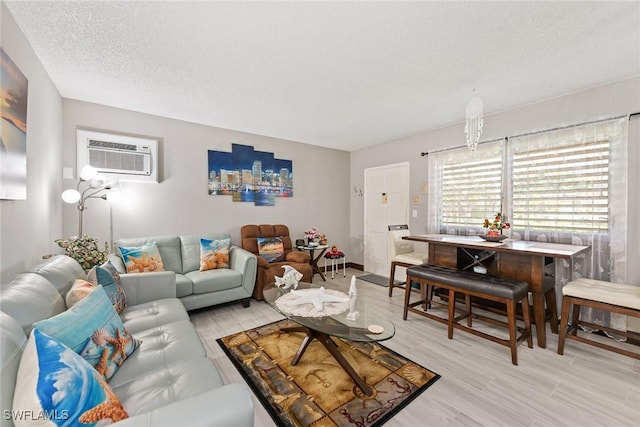 living room with a wall mounted air conditioner, a textured ceiling, and light wood-type flooring