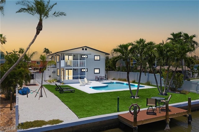 back house at dusk featuring a fenced in pool, a patio, a balcony, and a yard