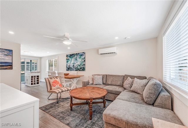 living room with an AC wall unit, ceiling fan, and light hardwood / wood-style flooring