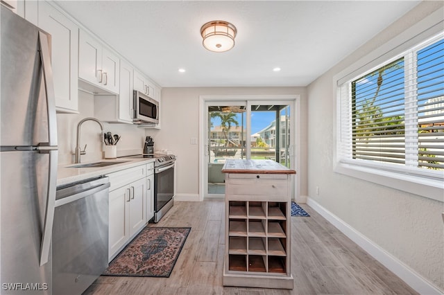 kitchen featuring appliances with stainless steel finishes, sink, light hardwood / wood-style flooring, and white cabinets